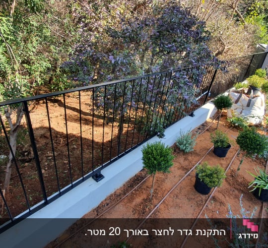 גדר ממתכת שחורה המותקנת על גבי חומת בטון בגינה